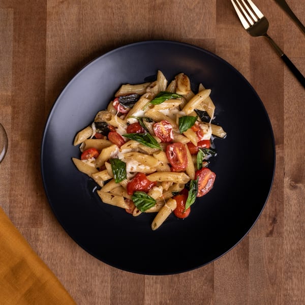 Edoardo's penne pasta with cherry tomatoes, mozzarella, and basil on a black plate.