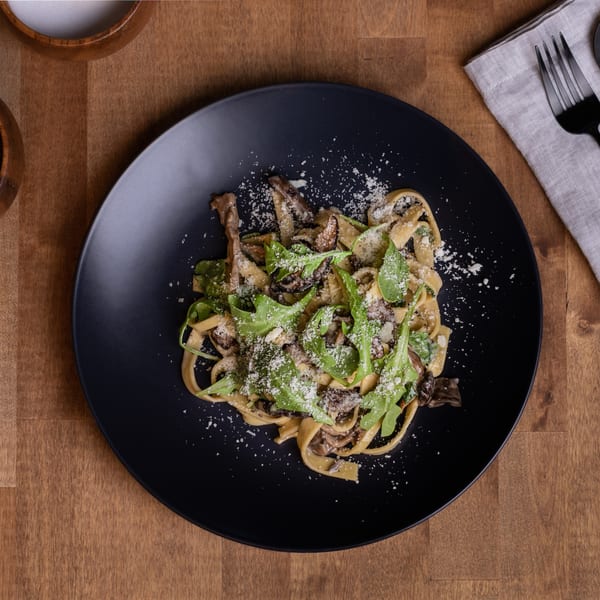 Edoardo's Trattoria's tagliatelle pasta with mushrooms, arugula, and grated cheese on a black plate.