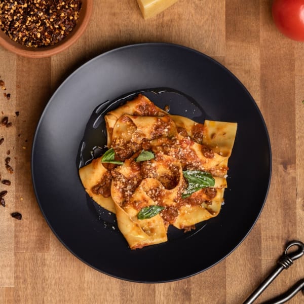 Edoardo's Trattoria's pappardelle pasta with bolognese sauce, parmesan, and basil on a black plate.