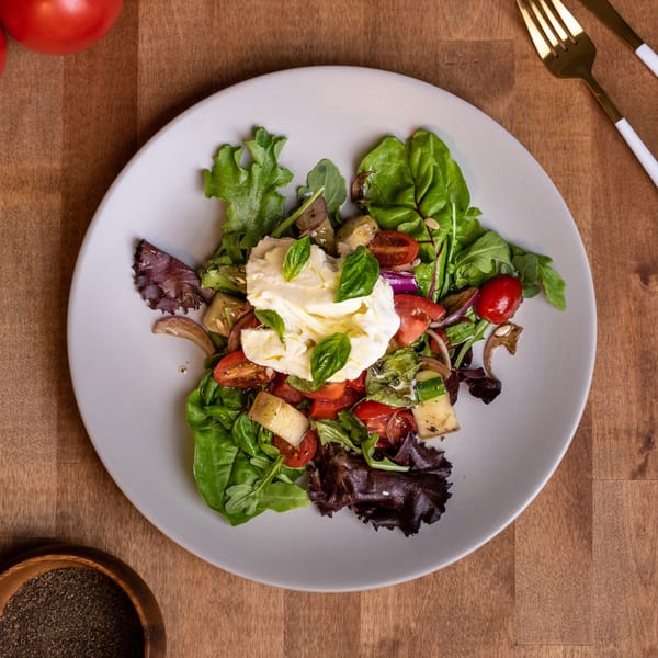 Edoardo's Trattoria's fresh Italian salad with burrata, cherry tomatoes, and mixed greens on a white plate.