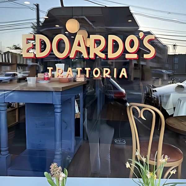 Edoardo's Trattoria sign on a window reflecting the street, with interior tables visible.