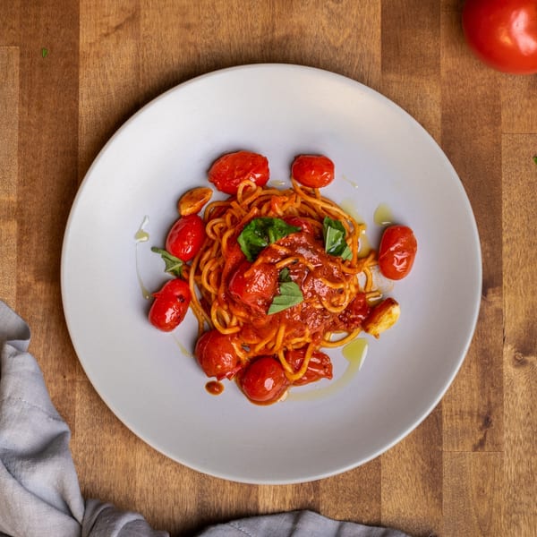 Edoardo's Trattoria's spaghetti with tomato sauce, cherry tomatoes, basil, and garlic on a white plate.